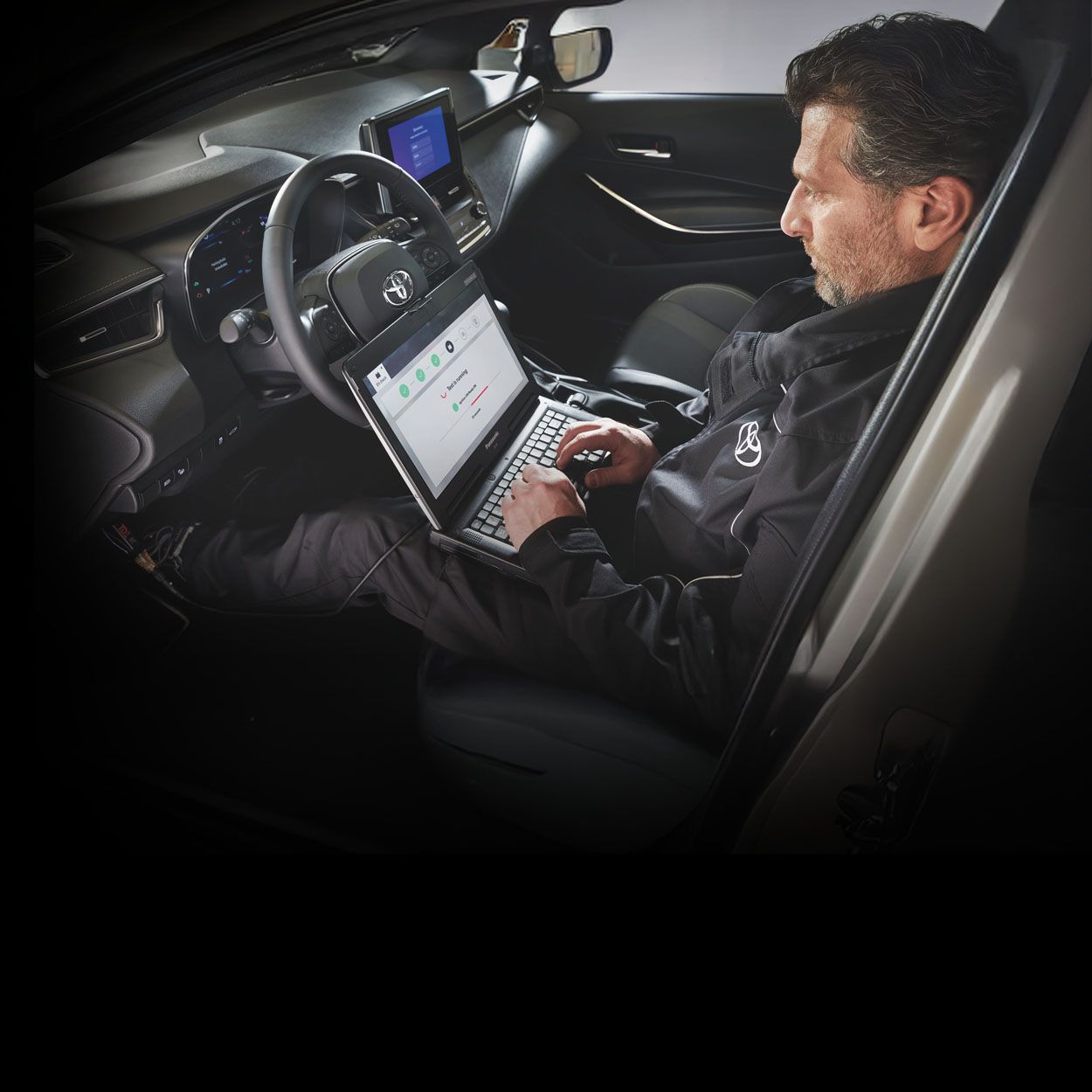 Ein Mechaniker sitzt auf dem Fahrersitz eines Toyota und liest auf seinem Computer, den er auf dem Schoß hat, die Fehlermeldungen des Autos aus.