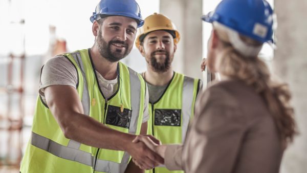 Eine Person mit Helm und gelber Warnweste schüttelt die Hand einer Person mit langen Haaren.