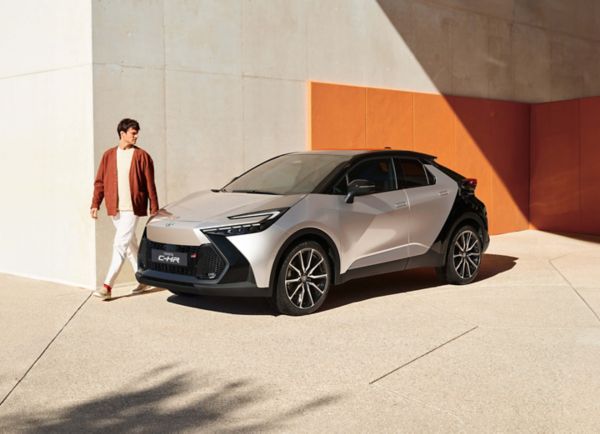 Person läuft an einem silber-schwarzen Toyota C-HR entlang, der vor einer orange-weißen Wand steht