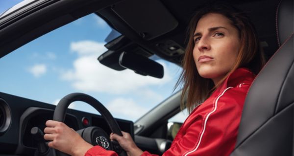 Eine Person in roter Jacke sitzt am Steuer eines Toyotas und schaut aus dem Fenster heraus