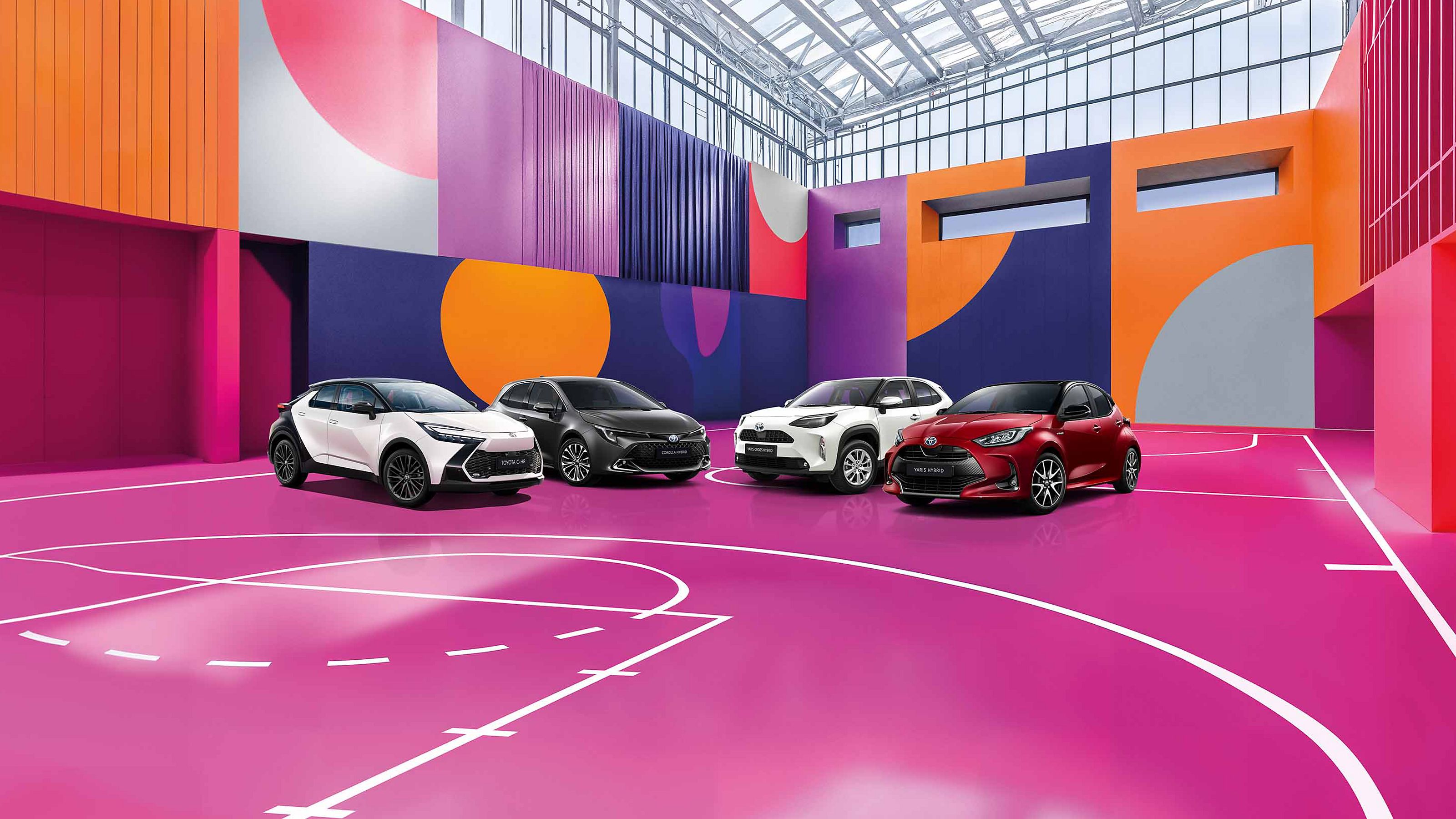Vier Toyota Fahrzeuge auf dem Innenhof eines modernen Gebäudes mit Glasfront, Bildtext: „LAST MINUTE DEALS, 1,99% EASY FINANZIERUNG“