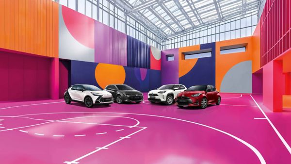 Ein weißer Toyota C-HR, ein grauer Corolla, ein weißer Yaris Cross und ein roter Yaris stehen auf einem bunten, mit lilanen, roten und blauen Mustern versehenen Basketballplatzes