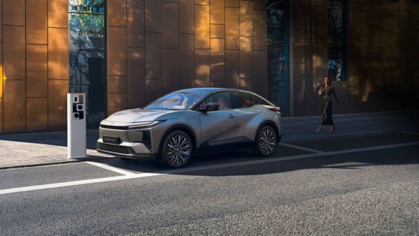 Ein silberner Toyota C-HR+ parkt an einer Straße in der Innenstadt neben einer Ladesäule.
