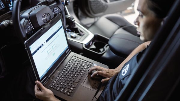 Ein Toyota-Mitarbeiter sitzt auf dem Fahrersitz eines Toyota und arbeitet am Laptop auf seinem Schoß. 