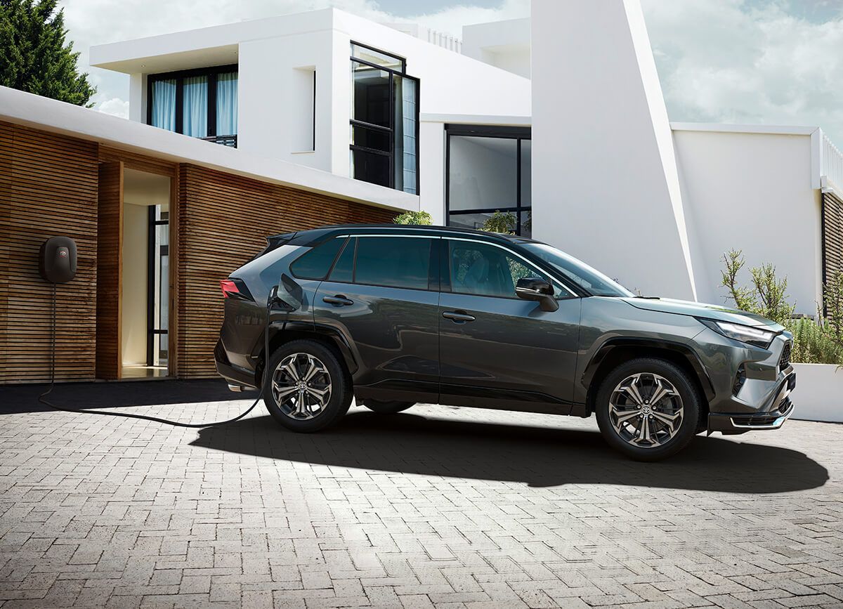 Ein dunkelgrauer Plug-in Hybrid SUV von Toyota steht auf einer Garageneinfahrt und lädt an einer Wallbox.