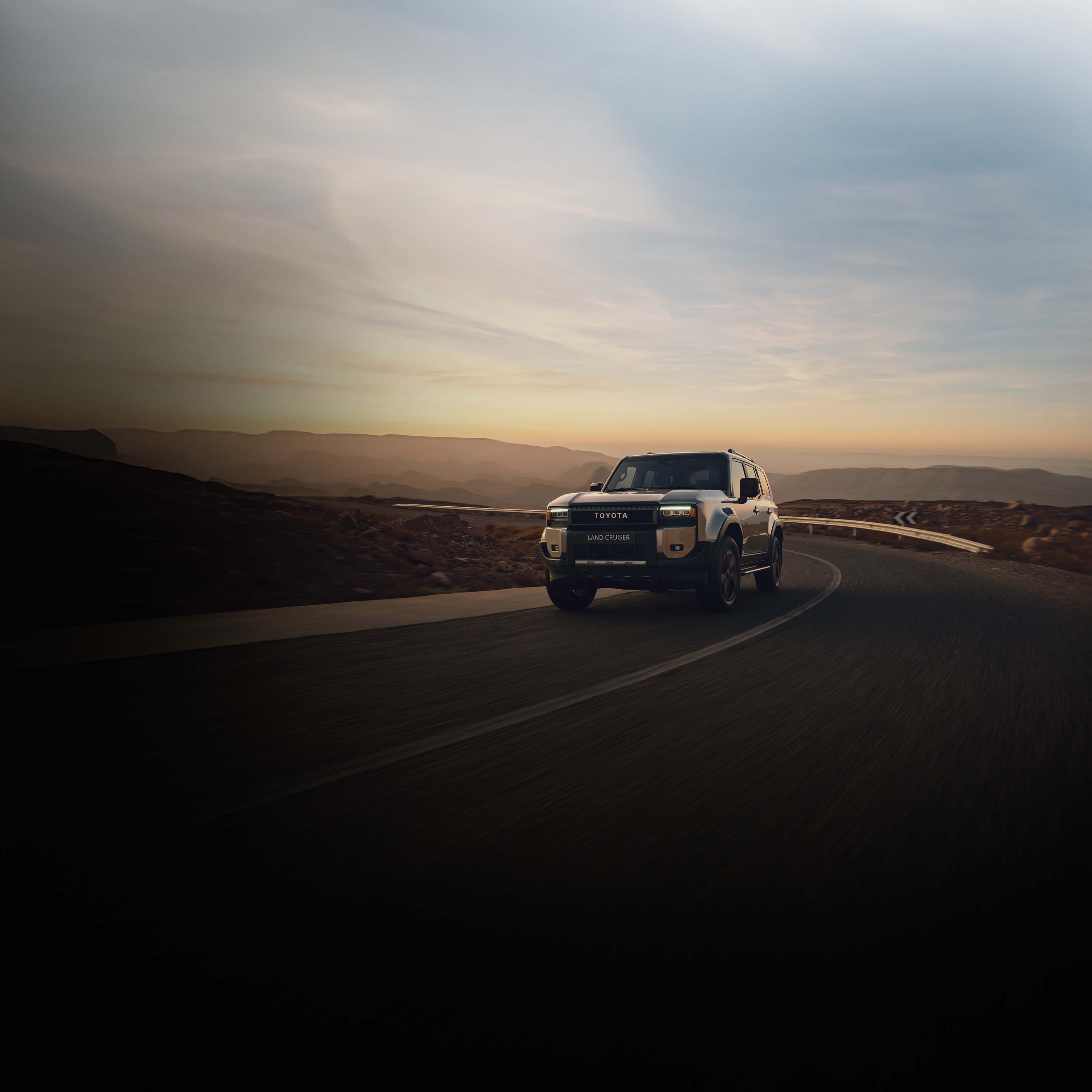 Sandfarbener Toyota Geländewagen fährt auf einer Landstraße durch felsige Wüstenlandschaft.