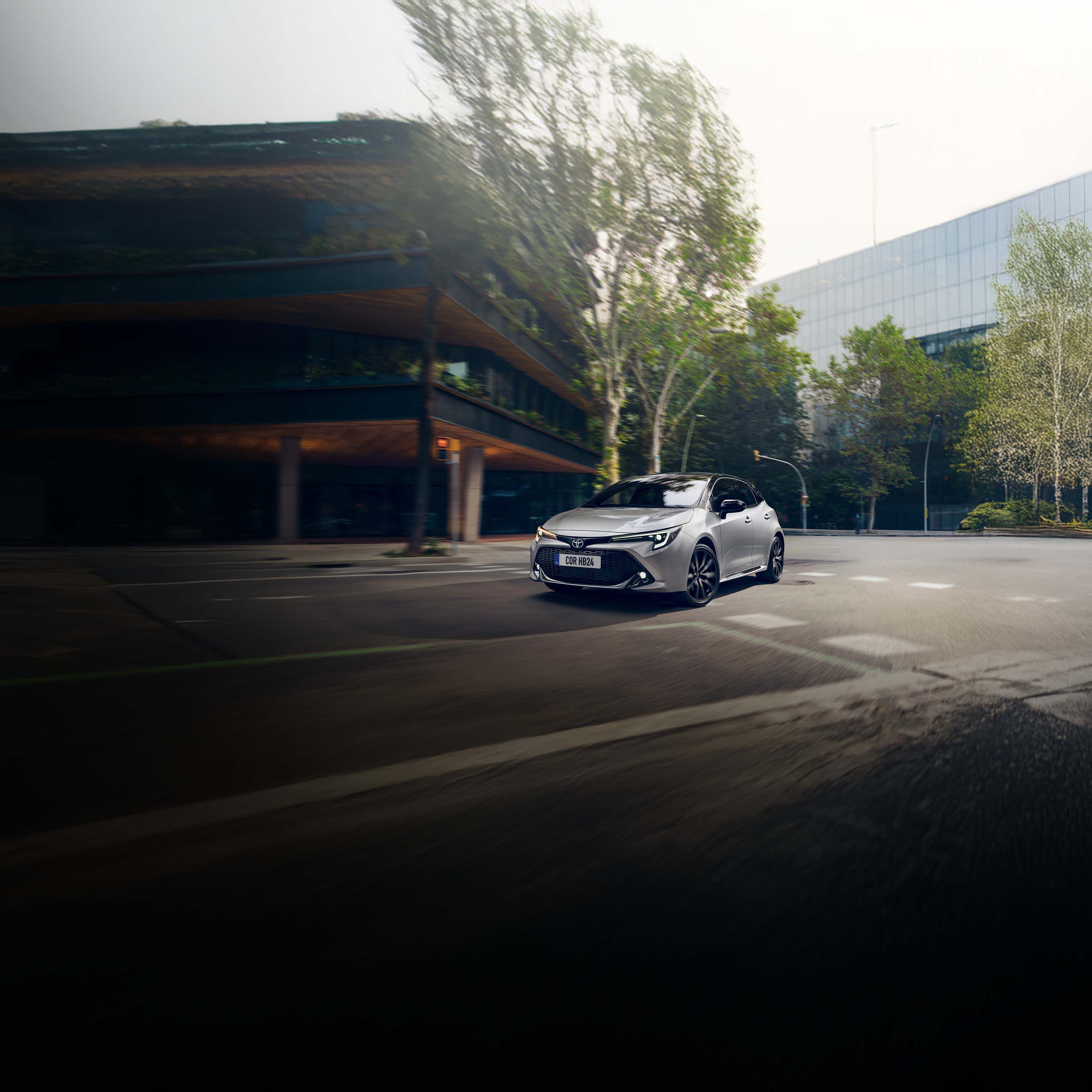 Silberner Toyota Kombi fährt um eine Kurve in einer begrünten Innenstadtumgebung.