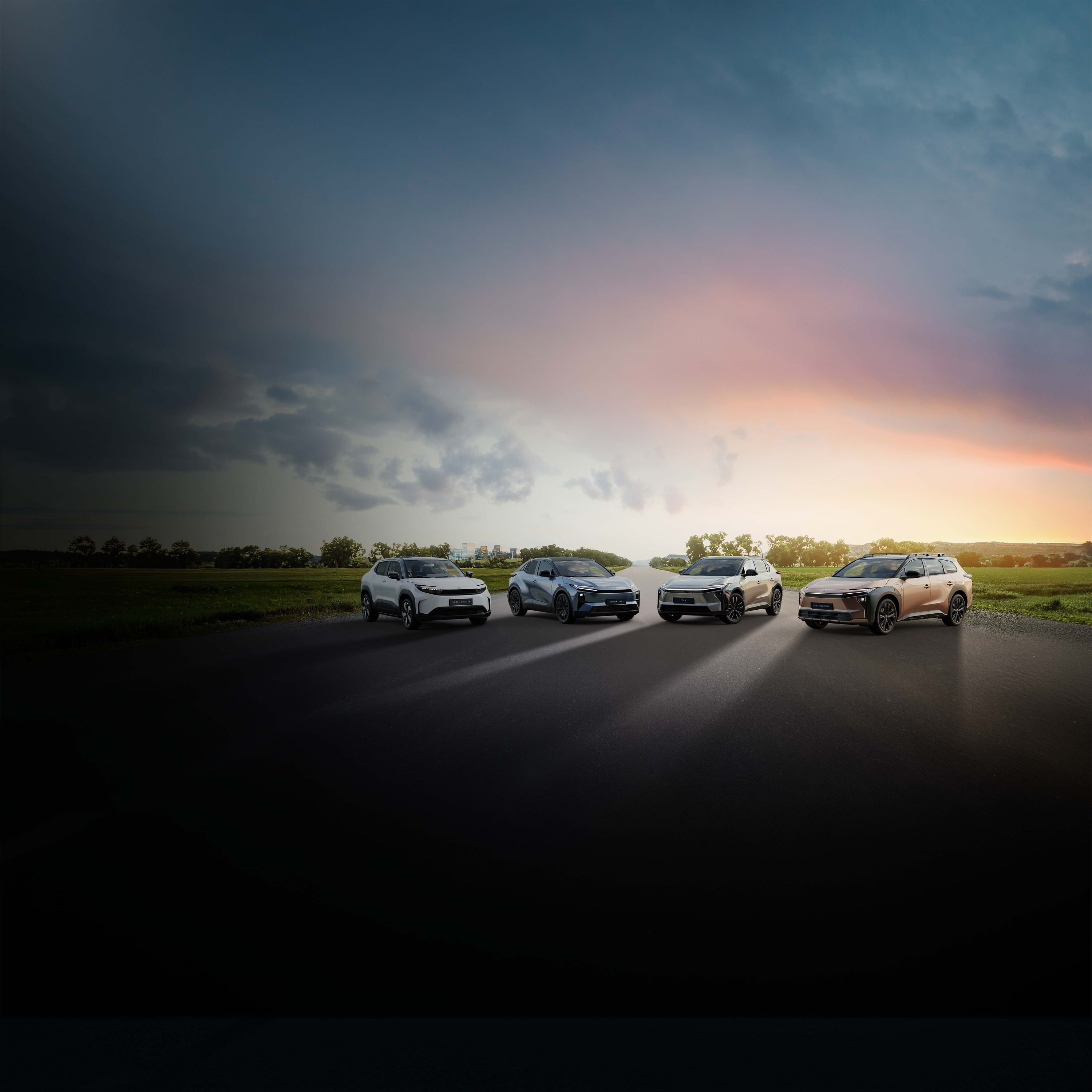 Vier Toyotas auf einer Straße vor weitläufiger Landschaft bei Sonnenuntergang, mit dramatischem Himmel und Lichtstimmung zwischen Dunkelheit und Abendsonne.