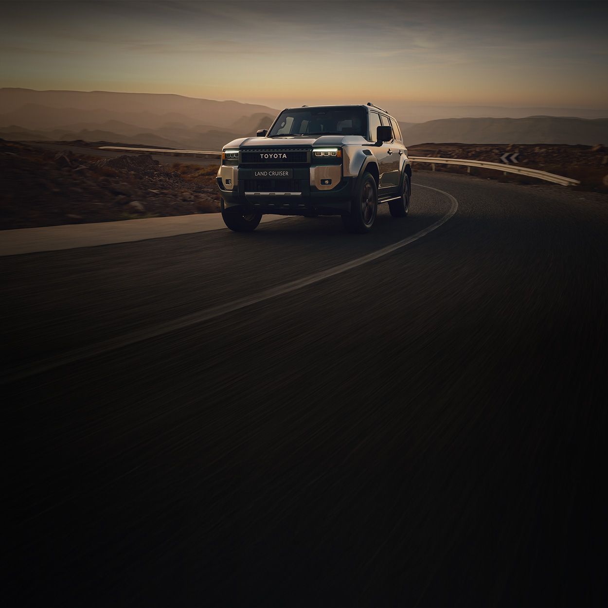 Sandfarbener Toyota Geländewagen fährt auf einer Landstraße durch felsige Wüstenlandschaft.