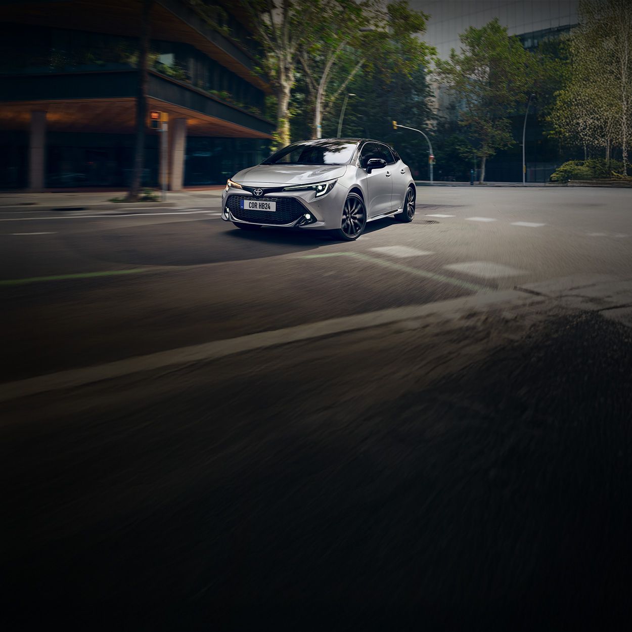 Silberner Toyota Kombi fährt um eine Kurve in einer begrünten Innenstadtumgebung.