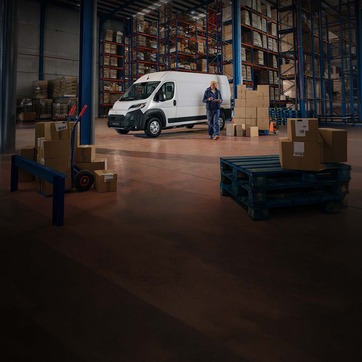 Toyota Proace Transporter steht in einer Lagerhalle zwischen Regalen und Versandkartons.