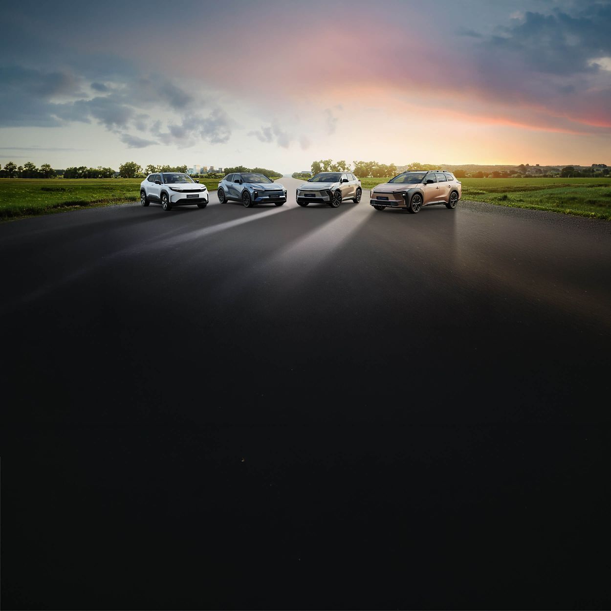 Vier Toyotas auf einer Straße vor weitläufiger Landschaft bei Sonnenuntergang, mit dramatischem Himmel und Lichtstimmung zwischen Dunkelheit und Abendsonne.