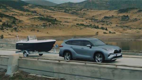 Toyota Highlander schleppt ein Boot auf einem Anhänger hinter sich und fährt über eine Brücke.