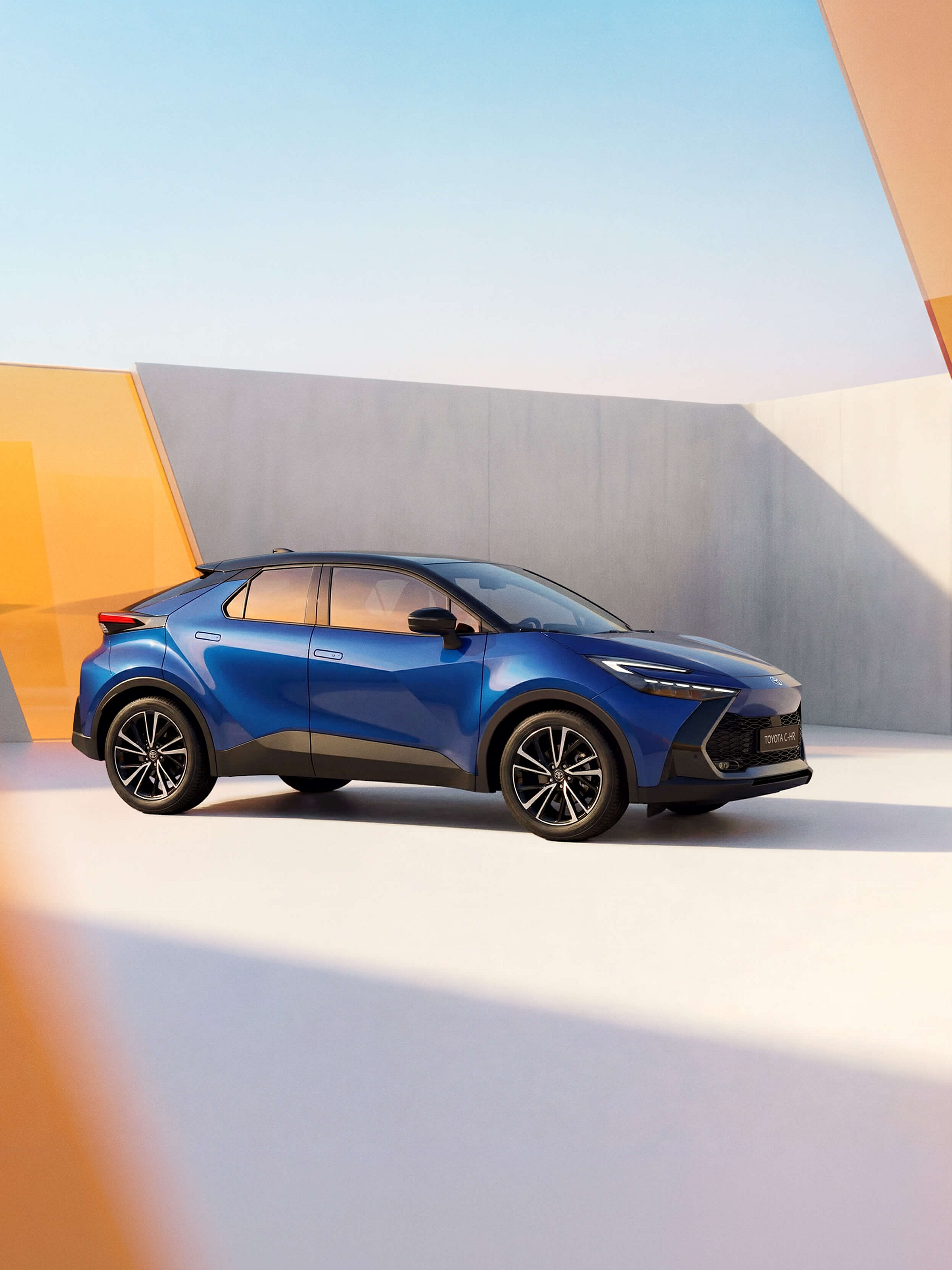Blauer Toyota C-HR in moderner Architekturkulisse mit geometrischen Formen und warmem Licht.