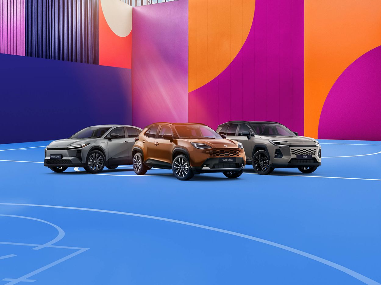 Vier Toyota-Fahrzeuge in Schwarz, Orange und Grau vor einem farbigen, grafischen Hintergrund, nebeneinander auf einer stilisierten Fläche präsentiert.
