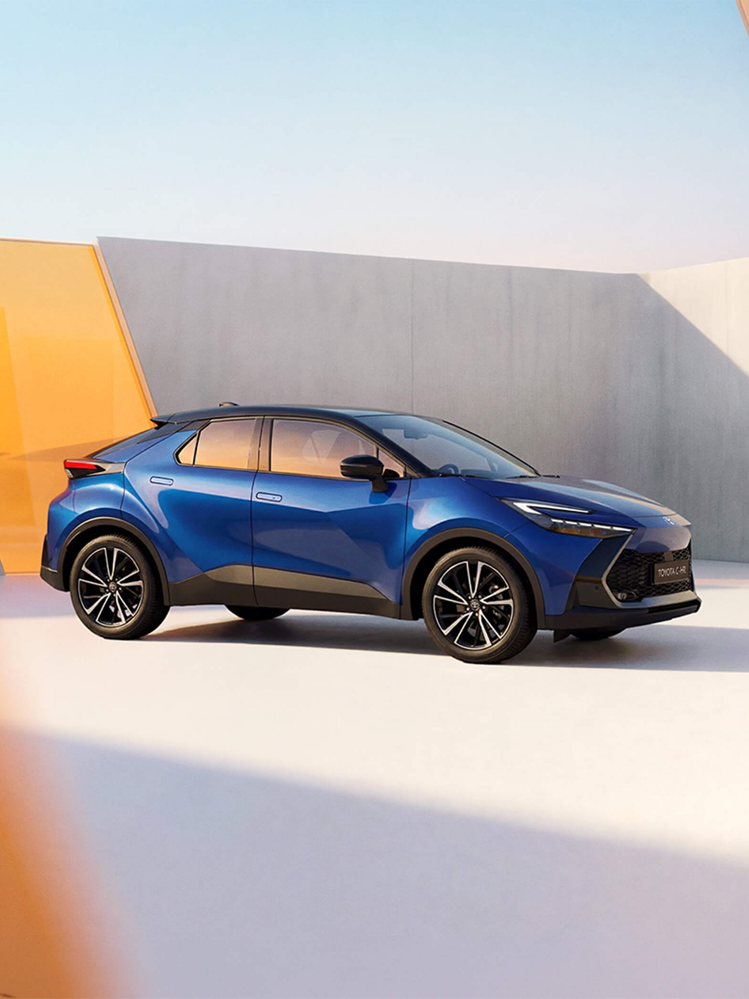 Blauer Toyota C-HR in moderner Architekturkulisse mit geometrischen Formen und warmem Licht.