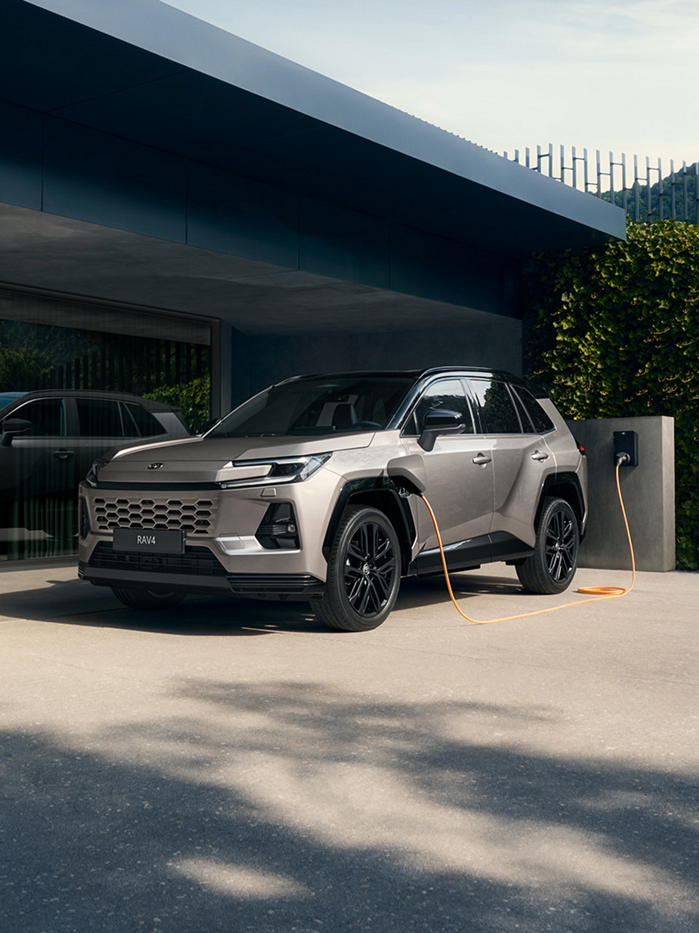 Silbernes RAV4 lädt an Wallbox vor modernem Haus.