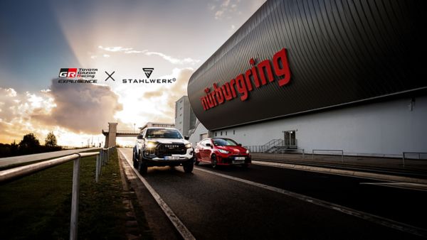 Zwei Toyota-Fahrzeuge vor dem Nürburgring-Gebäude mit rotem Schriftzug, Logos von Toyota GR Racing Experience und Stahlwerk im Himmel.