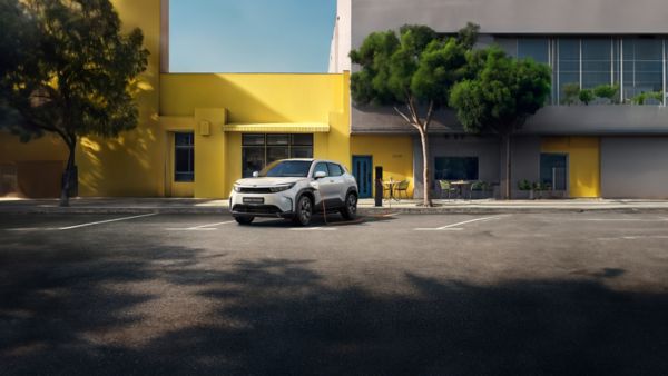 Ein weißer Kompakt-SUV parkt auf der städtischen Straße vor einem gelben Haus und lädt an einer Ladesäule.