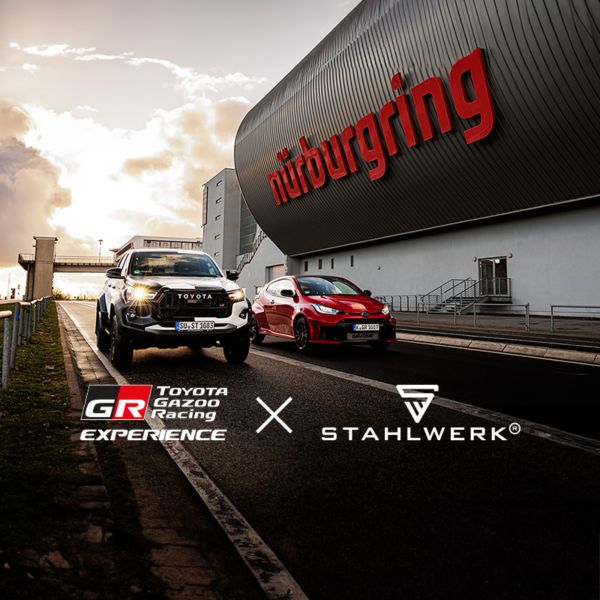 Zwei Toyota-Fahrzeuge vor dem Nürburgring-Gebäude mit rotem Schriftzug, Logos von Toyota GR Racing Experience und Stahlwerk im Himmel.