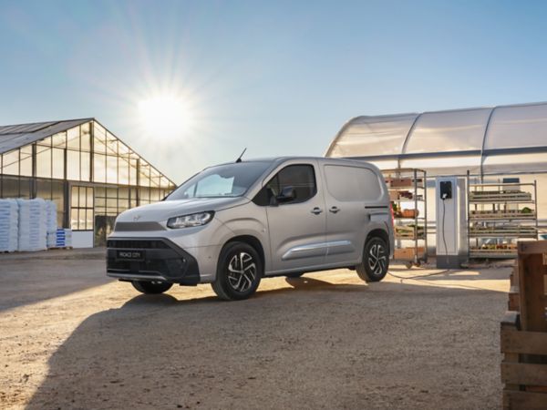 Ein silberner Toyota Kastenwagen steht zwischen Gewächshäusern und lädt an einer Wallbox.
