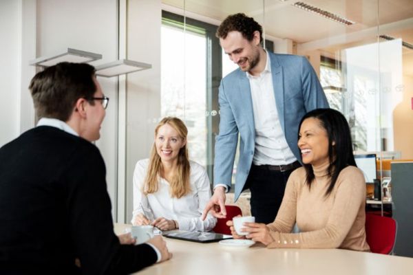 Vier Arbeitskollegen sitzend lachend an einem Bürotisch in einem Meeting