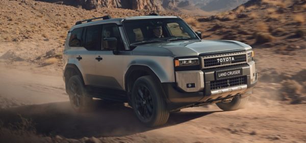 Silberner Land Cruiser fährt auf einer unbefestigten Straße entlang. Im Hintergrund sieht man eine steinige Umgebung.
