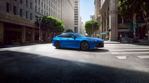 Ein blauer Mirai steht auf einer Straße umgeben von Hochhäusern und Bäumen im Hintergrund.