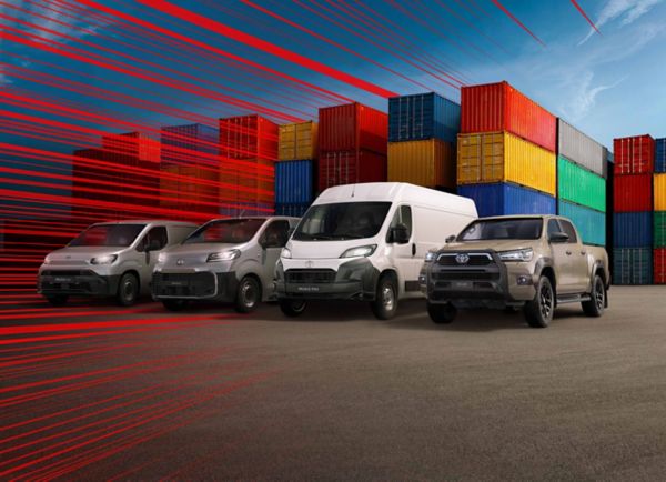 Hilux, Proace Max, Proace und ein Proace City schräg von vorn auf einem Parkplatz, umgeben von Stapeln aus Europaletten, daneben Ladesäulen