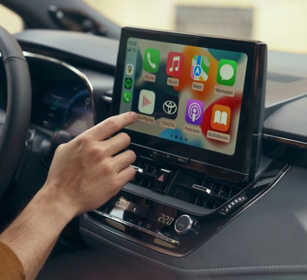 Person tippt auf den Bildschirm eines Multimediabildschirms auf dem mehrere Apps wie Nachrichten, Musik und Navigation dargestellt sind.