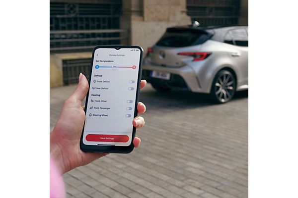 Person mit Smartphone in der Hand steht vor einem geparkten Toyota. Auf dem Bildschirm ist die MyToyota App geöffnet auf der die Temperatur angezeigt wird.