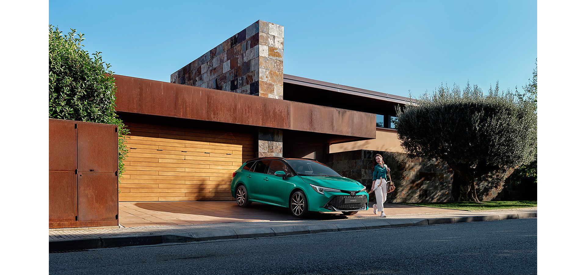 Woman walking out of a modern house, and around a parked green Toyota Corolla