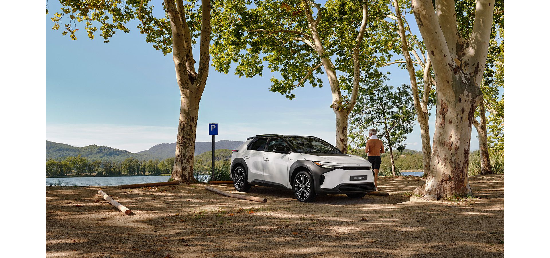 White bz4X parked overlooking a natural landscape. Man stood next to the car admiring the view 