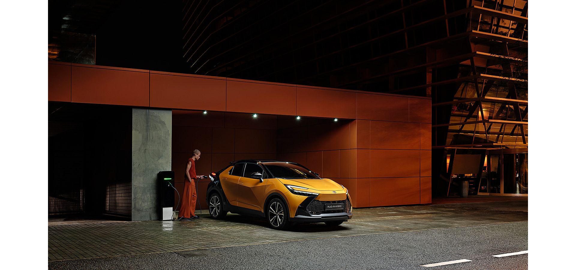 Man wearing fashionable orange outift stood by orange C-HR, outside of a dimly lit parking garage.