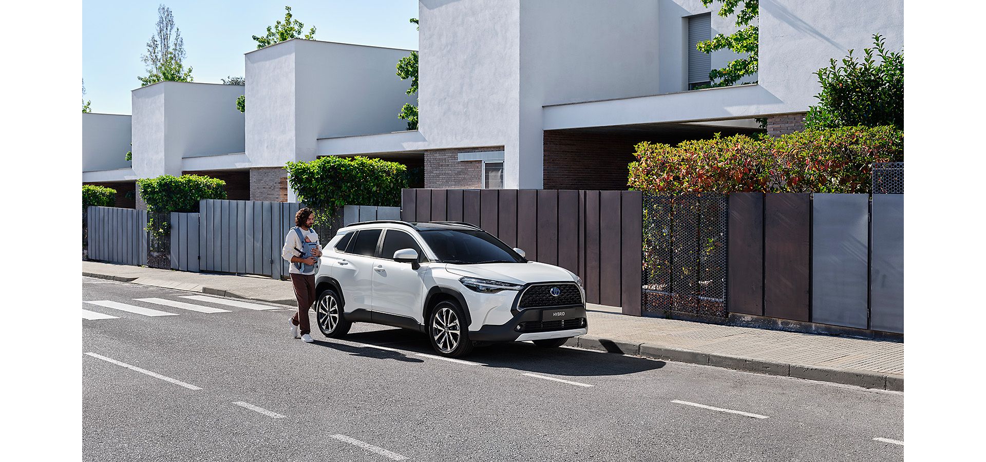 Man with a child, leaving their modern house, walking towards their parked white Corolla Cross,