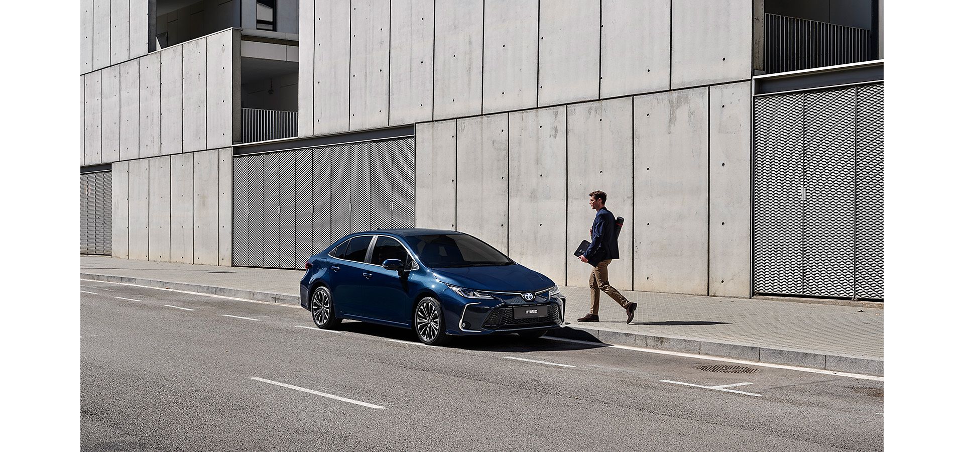 Business man walking towards their navy blue Corolla Sedan, which is parked outside of a modern building