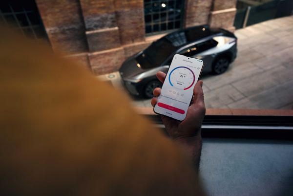 Person hält ein Smartphone in der Hand auf der die MyToyota App geöffnet ist, im Hintergrund steht ein SUV auf einer Straße.