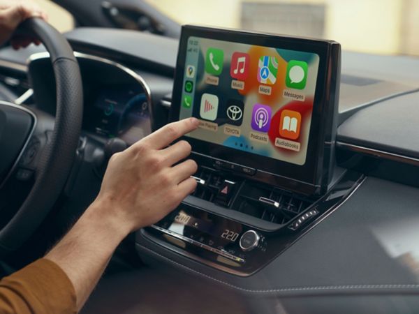 Person tippt auf den Bildschirm eines Multimediabildschirms auf dem mehrere Apps wie Nachrichten, Musik und Navigation dargestellt sind.