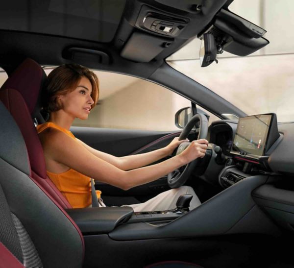 Seitliche Sicht auf eine Frau am Steuer eines Toyotas, die lächelnd und konzentriert nach vorne schaut.