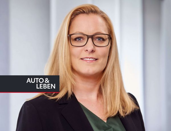 Portrait von Cathrin Koch mit langen, glatten blonden Haaren und Brille, die einen schwarzen Blazer über einem grünen Oberteil trägt
