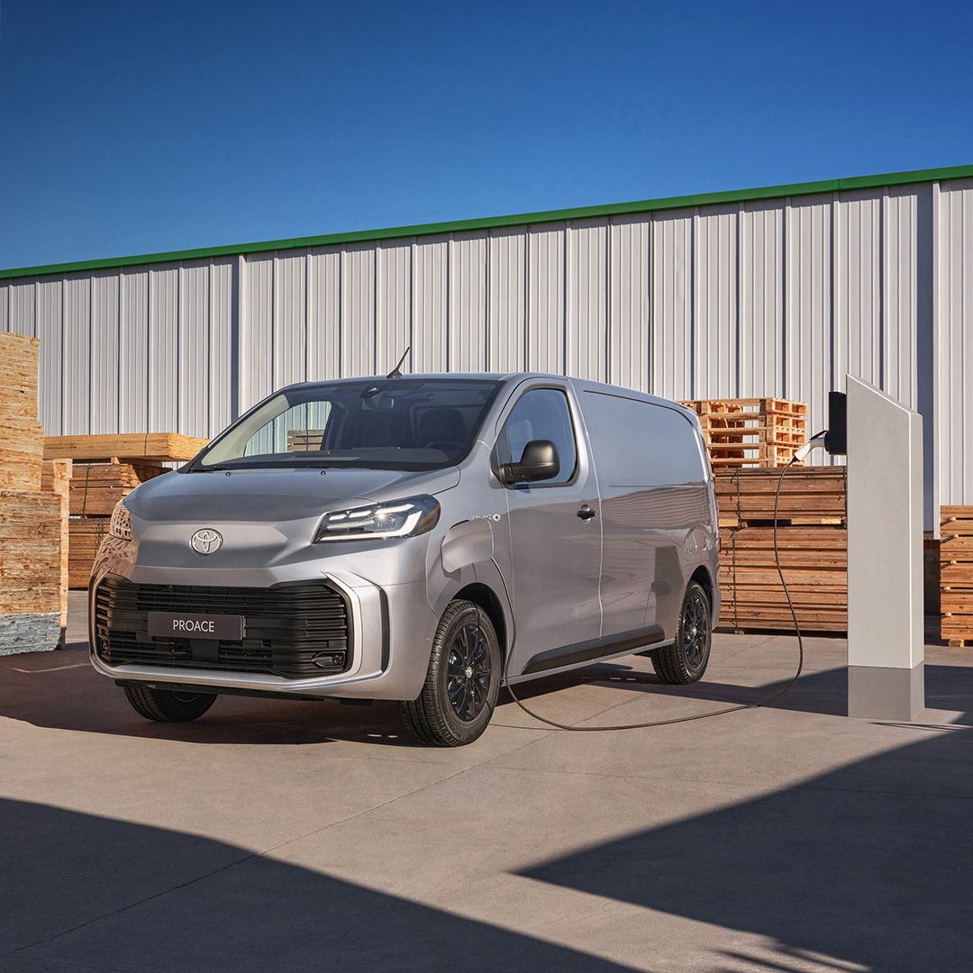 Ein grauer Proace Electric steht umgeben von Holz-Paletten an einer Ladesäule.