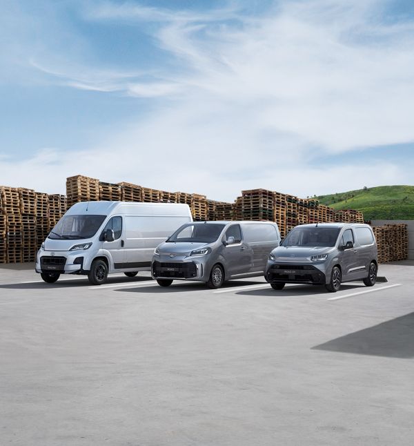 Toyota Proace Max, Proace Verso und Proace City nebeneinander vor gestabelten Paletten. Blauer Himmel mit einigen Wolken.