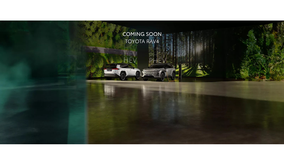 Twee witte Toyota RAV4 SUV's in een meeslepende bosomgeving, één aangesloten op een oplaadpunt. Tekst bovenaan de afbeelding "COMING SOON - TOYOTA RAV4”