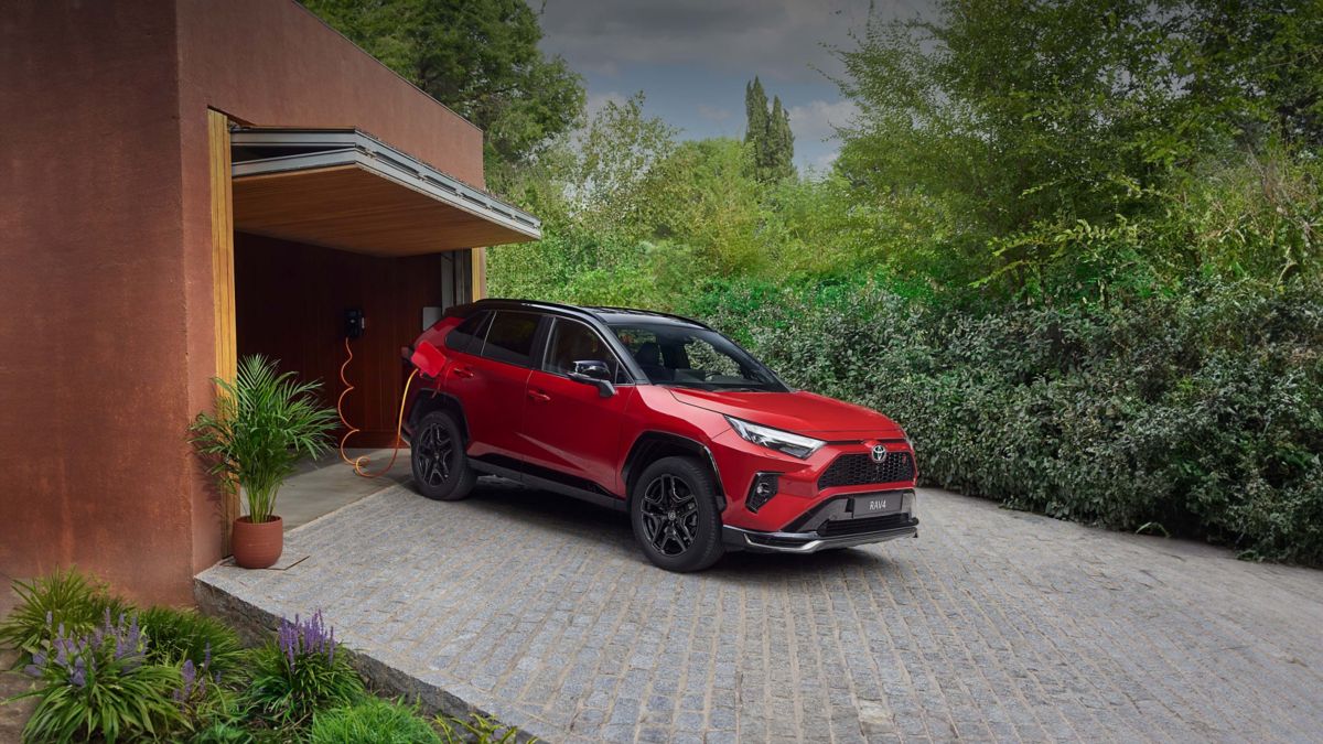 Grauer RAV4 steht vor einer Garage und ist mit einem Kabel an den Ladestation angeschlossen.