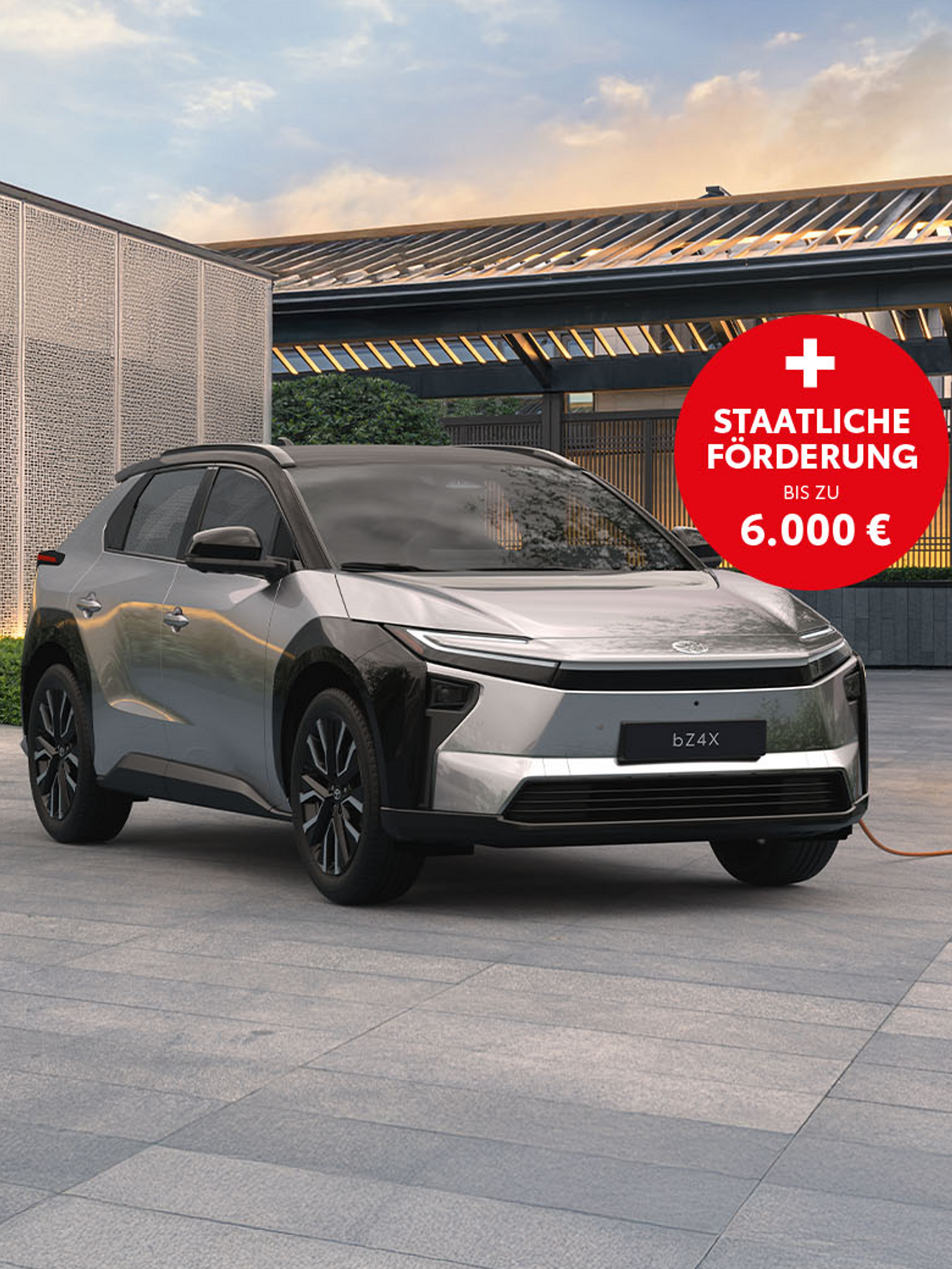 Toyota bZ4X in Silber lädt an einer Wallbox vor moderner Architektur bei Abenddämmerung.