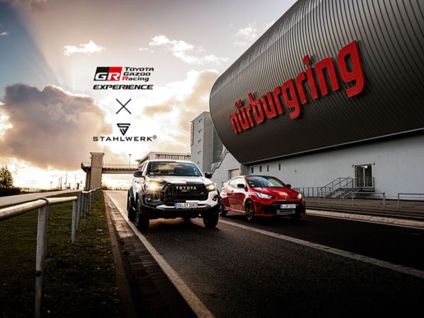 Ein roter GR Yaris und ein silberner, großer SUV von Toyota fahren neben einem Werbebanner mit dem Schriftzug "Nürburgring" über die Rennstrecke, während im Hintergrund das Logo Toyota Gazoo Racing und das Logo von Stahlwerk erscheinen
