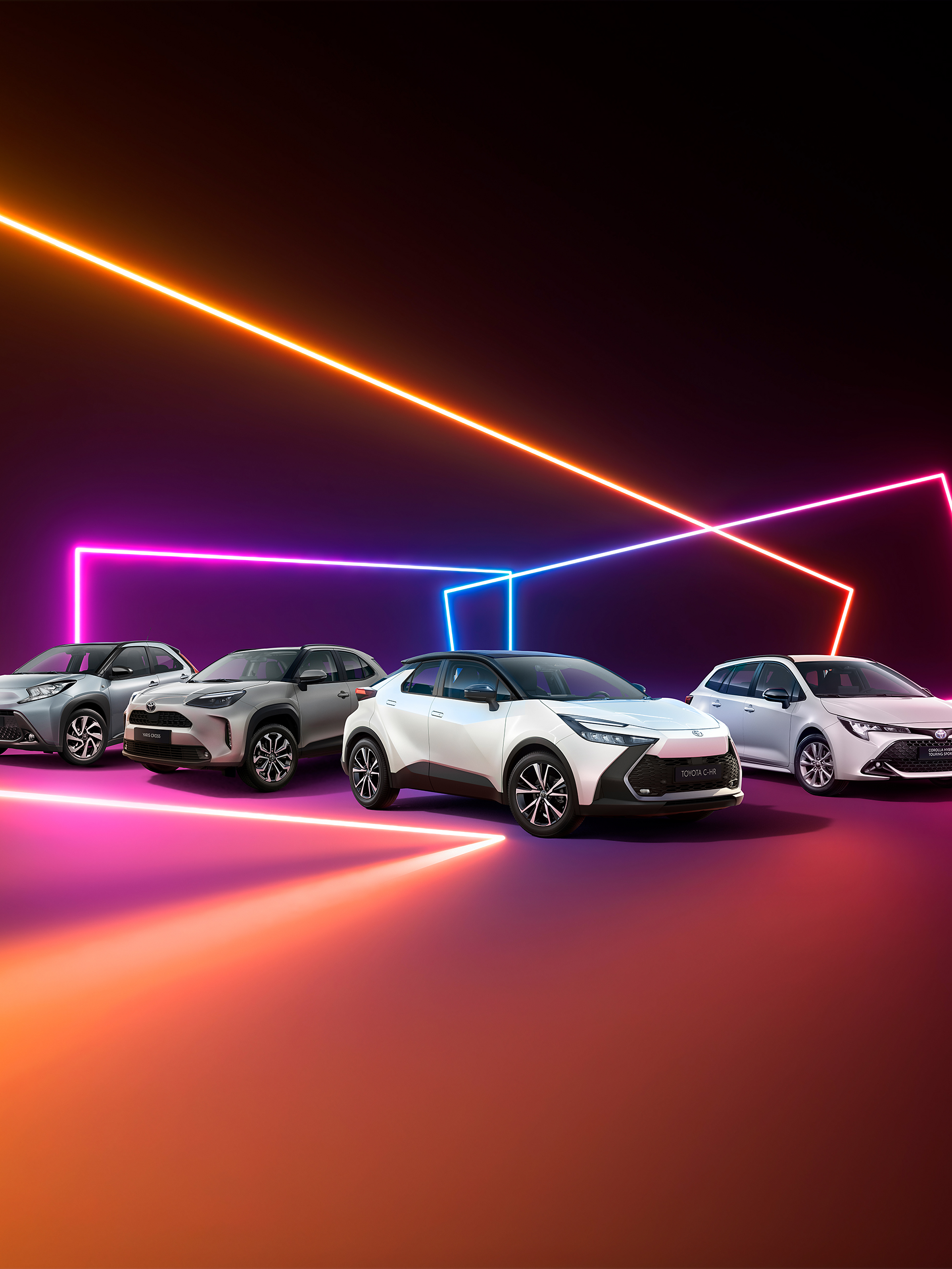 Vier Toyota Fahrzeuge stehen nebeneinander vor einem dunklen Hintergrund, umgeben von leuchtenden, farbigen Neonlinien in Orange, Pink und Blau, die eine dynamische, futuristische Szenerie erzeugen.