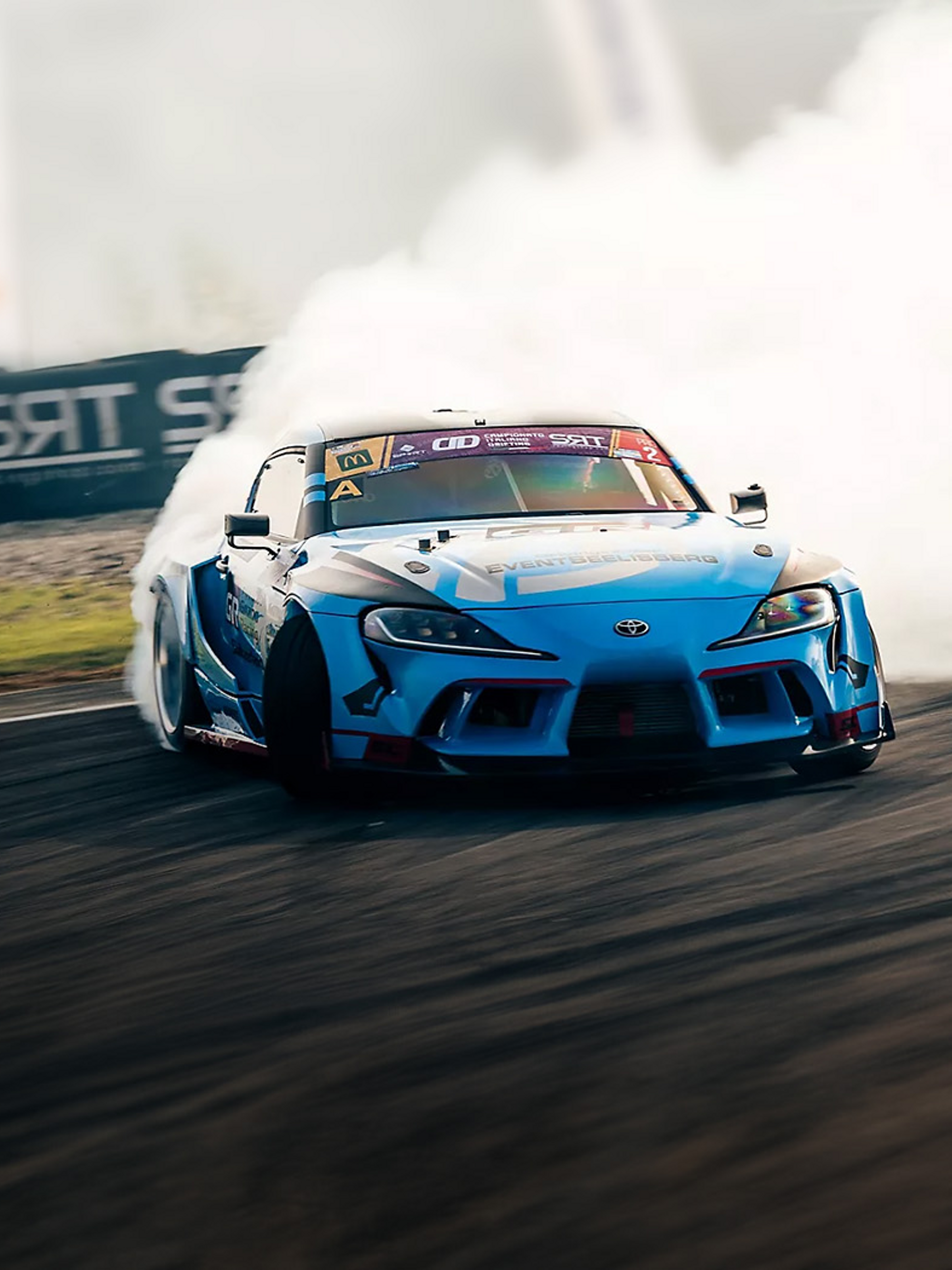 Blauer Sportwagen von Toyota driftet auf einer Rennstrecke um eine Kurve. Durch den Reifenabrieb entsteht weißer Qualm hinter dem Fahrzeug.