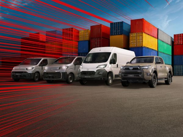 Hilux, Proace Max, Proace und ein Proace City schräg von vorn auf einem Parkplatz, umgeben von Stapeln aus Europaletten, daneben Ladesäulen