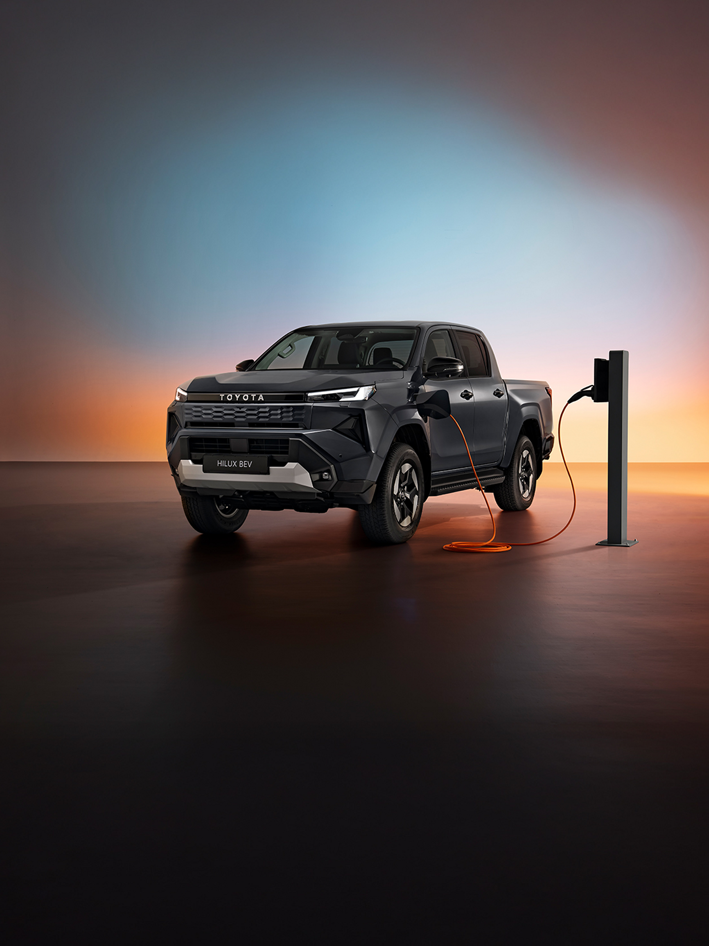 Seitenansicht des neuen vollelektrischen Toyota Hilux, der an einer Ladesäule lädt, mit buntem Hintergrund.